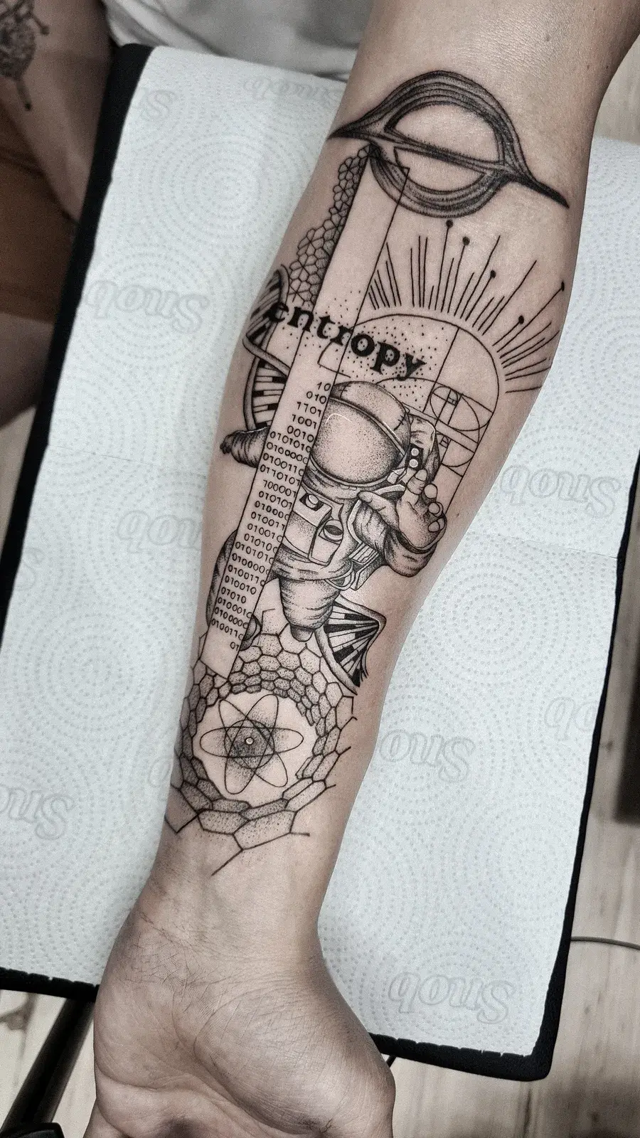 Tatuagem blackwork de astronauta com a palavra Entropy, DNA e geometria, em pontilhismo no antebraço