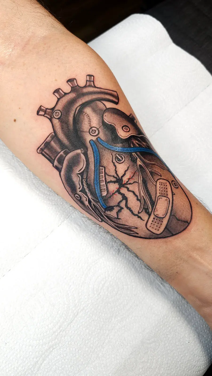 Tatuagem de coração anatômico com curativo e faixa azul no antebraço