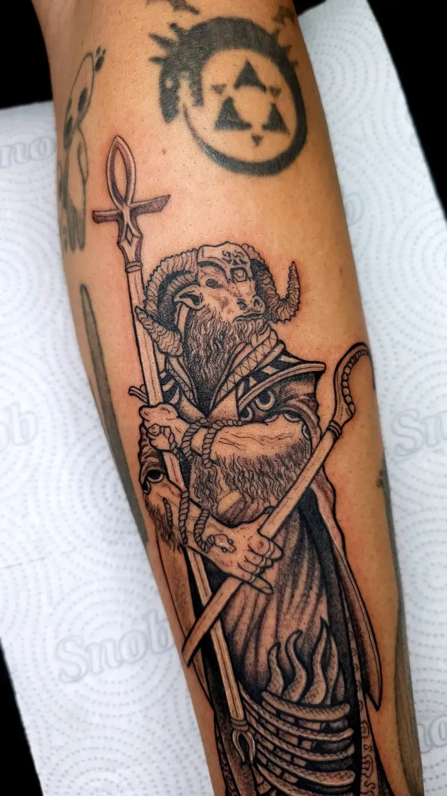 Tatuagem blackwork de divindade com chifres e cajado ankh, em pontilhismo no antebraço