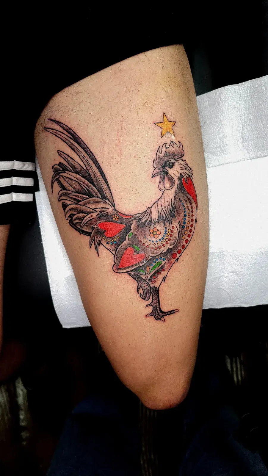 Tatuagem de galo de Barcelos com detalhes em cor e estrela amarela na coxa