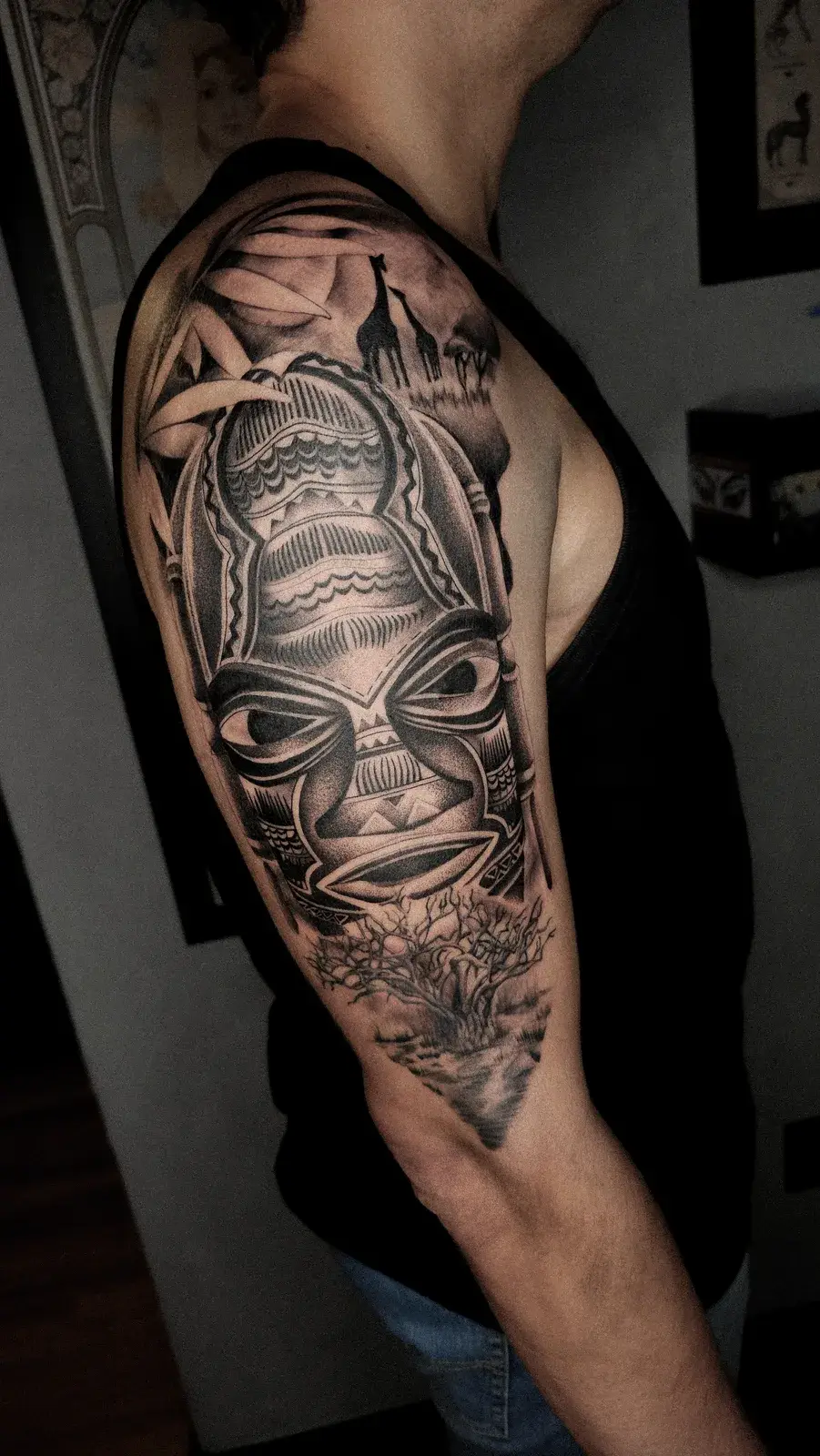 Tatuagem blackwork de máscara tribal ocupando o braço inteiro