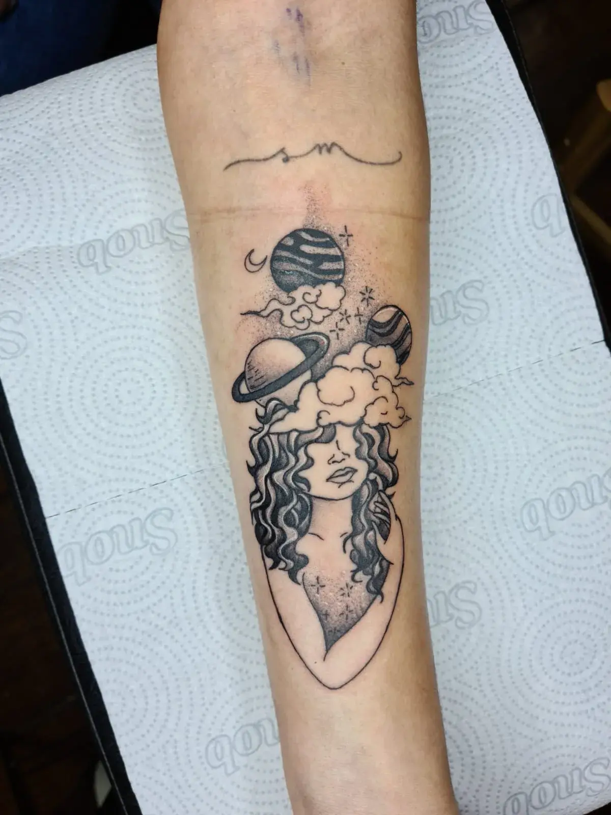 Tatuagem blackwork de mulher com cabelo de nuvens e planetas no antebraço, vista de perto