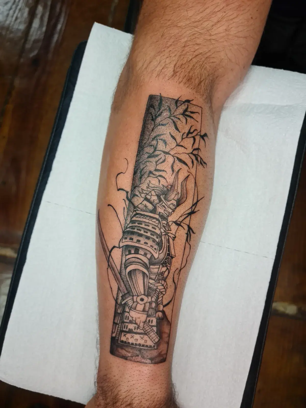 Tatuagem blackwork de elmo de samurai entre galhos secos, em pontilhismo no antebraço