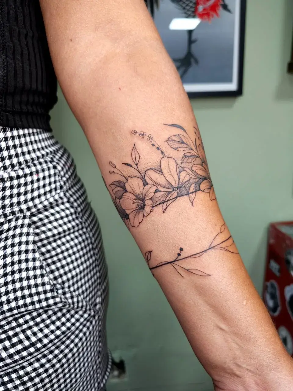 Tatuagem botânica em braçadeira floral com ramo fino contornando o antebraço, vista completa