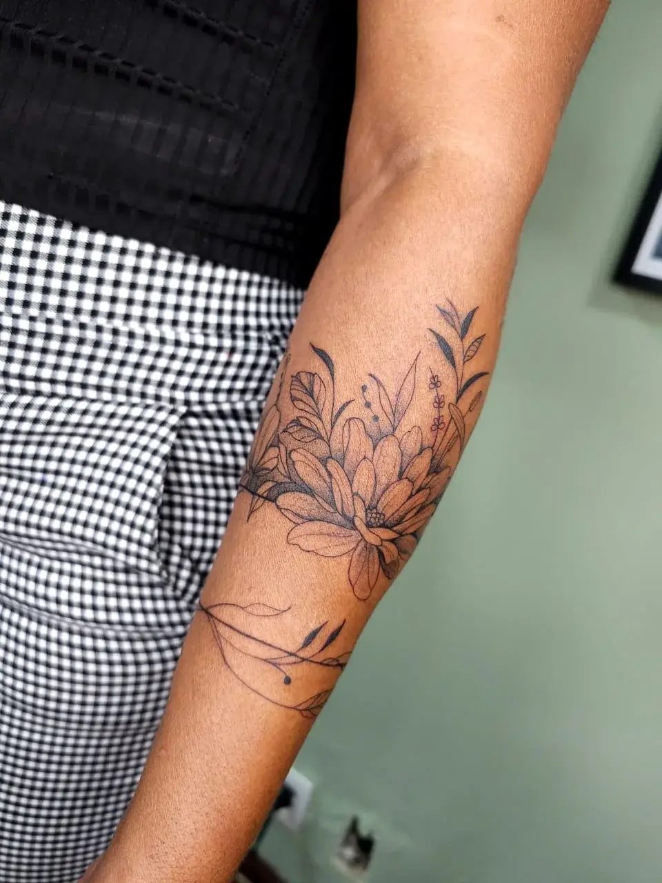 Tatuagem botânica em forma de braçadeira floral contornando o antebraço