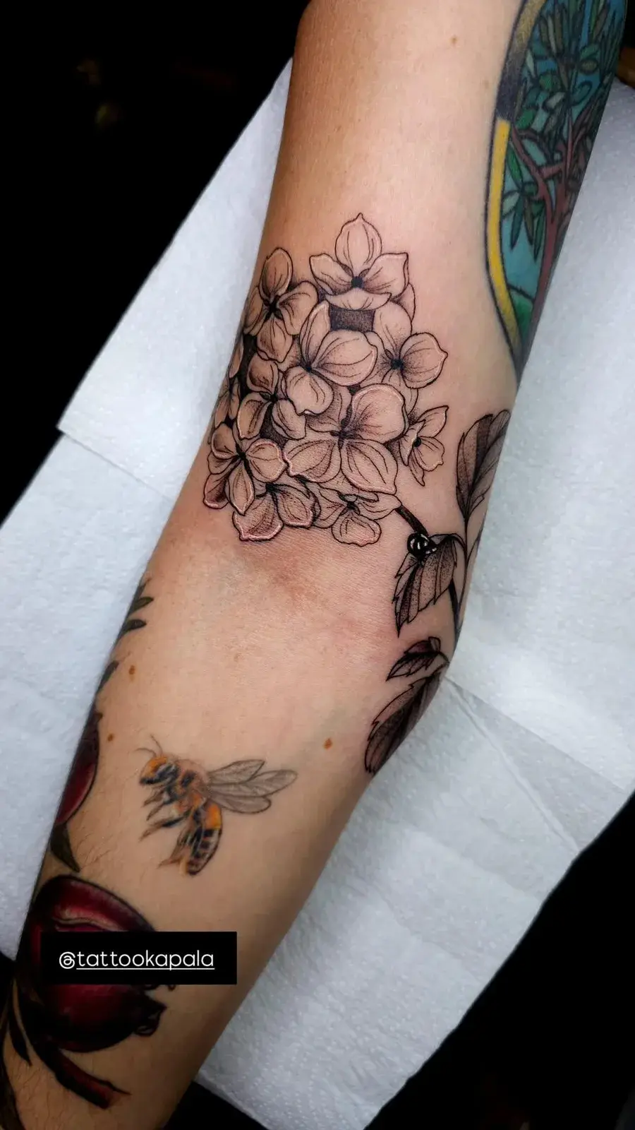 Tatuagem botânica de floral delicado em traço fino no braço, acima do cotovelo