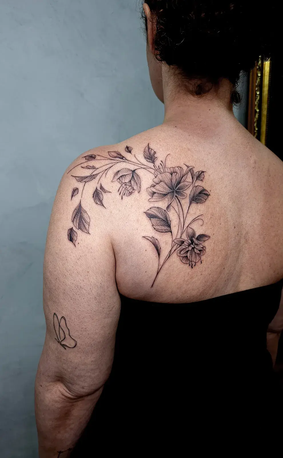 Tatuagem botânica com flores e folhas atravessando as costas e o ombro