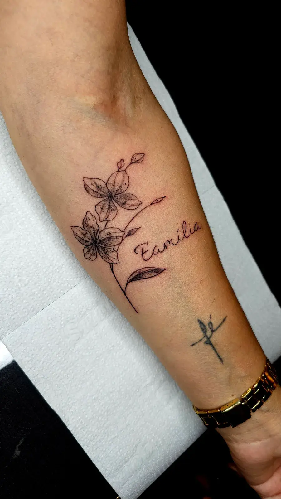 Tatuagem botânica com flores em traço fino e a palavra Família em lettering no antebraço