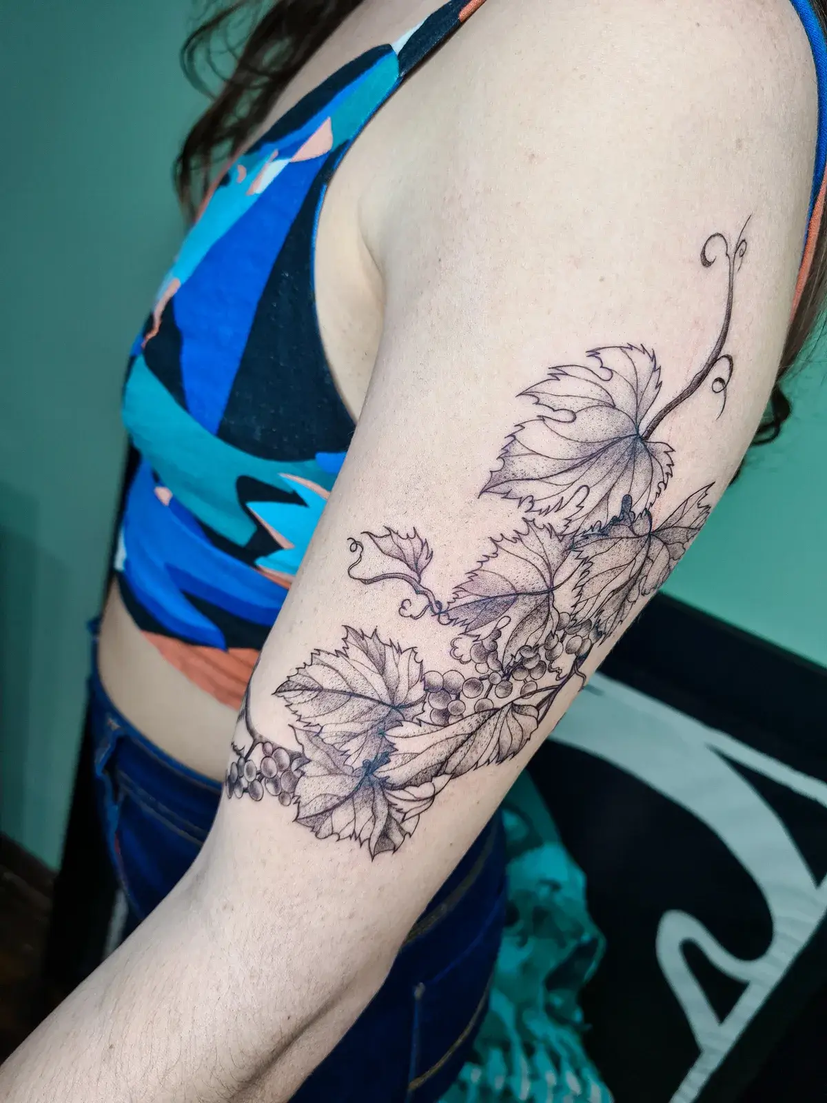 Tatuagem botânica de folhas e flores em traço fino no braço