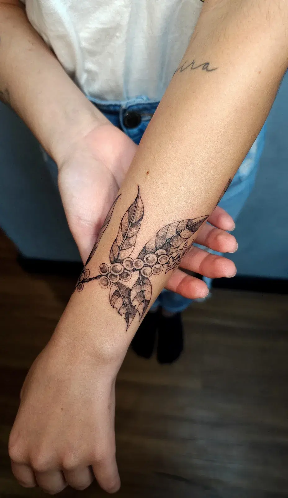 Tatuagem botânica de ramo de café com frutos e folhas em pontilhismo, contornando o punho