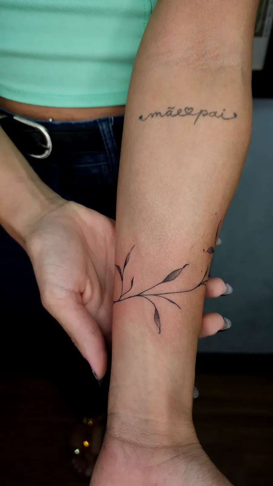 Tatuagem botânica de ramo com folhas dando a volta no antebraço, vista pelo lado interno