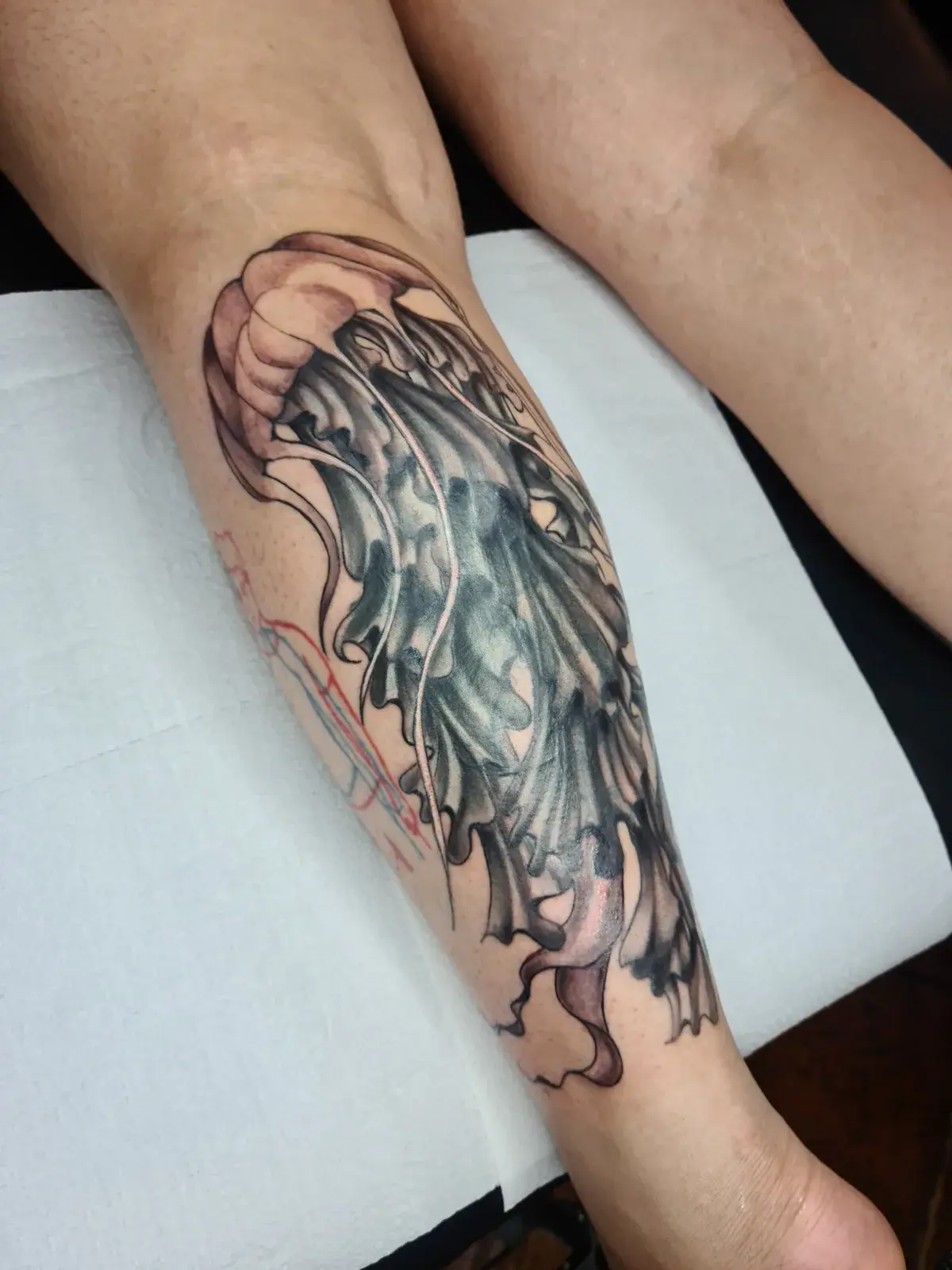 Cobertura de tatuagem com água-viva em preto e cinza na panturrilha, vista pela lateral da perna