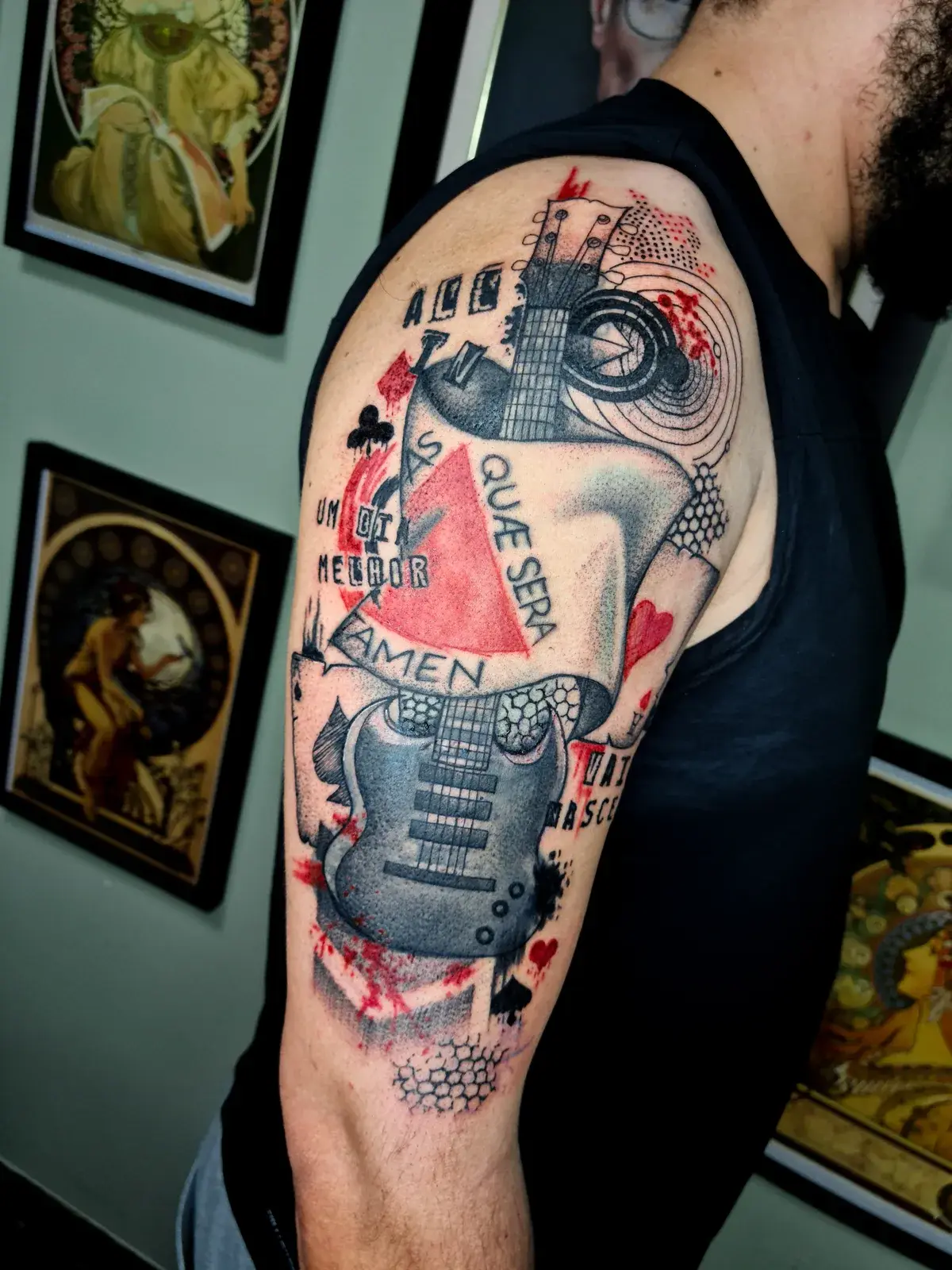 Cobertura de tatuagem em trash polka com guitarra, letras e respingos vermelhos no braço, do ombro ao bíceps