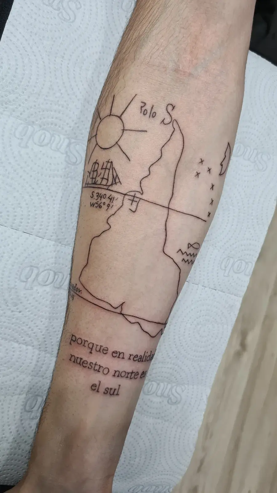 Tatuagem fine line com o mapa da América do Sul invertido e lettering em espanhol, no antebraço