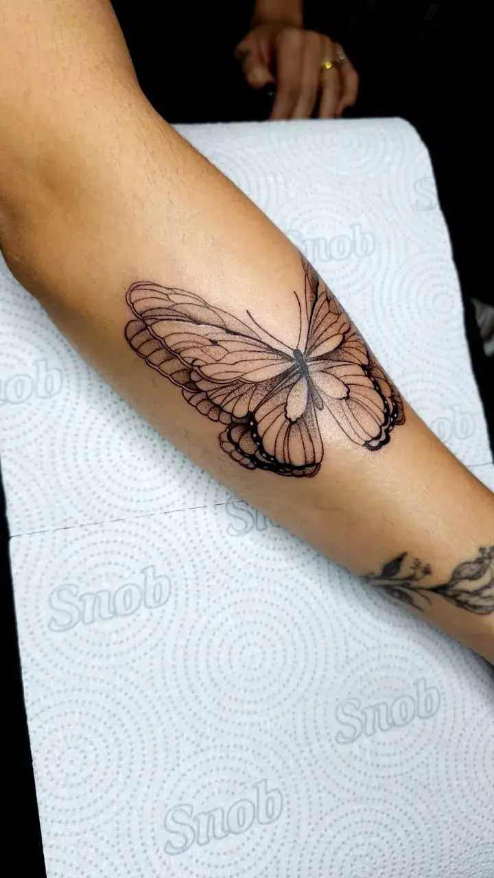 Tatuagem fine line de borboleta com asas detalhadas no antebraço