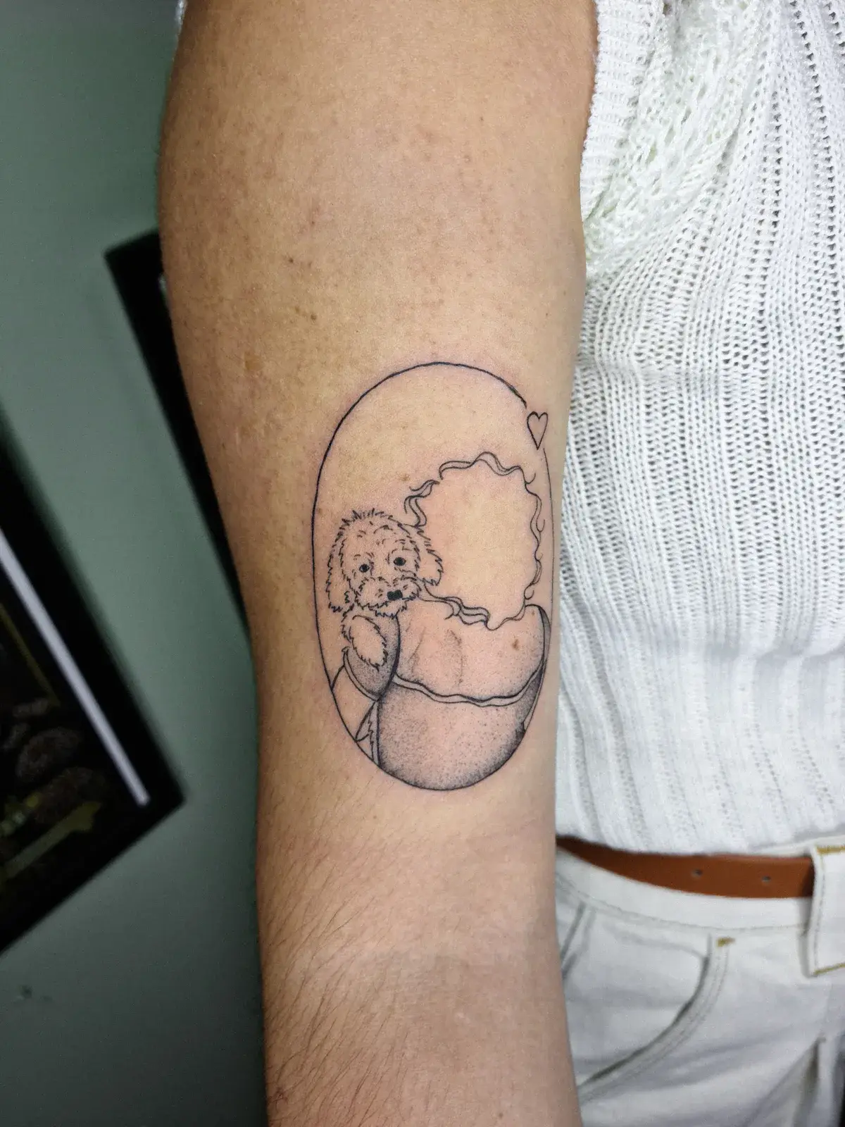 Tatuagem fine line de cachorro dentro de moldura oval, no braço