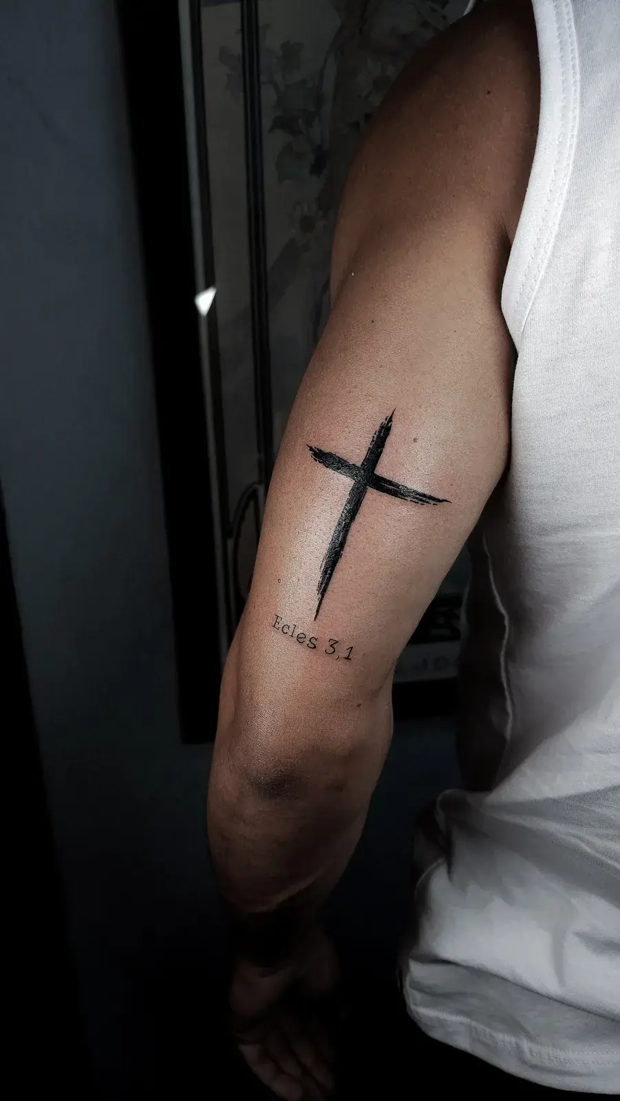 Tatuagem de cruz em traço pincelado e preto sólido, com referência bíblica, no braço