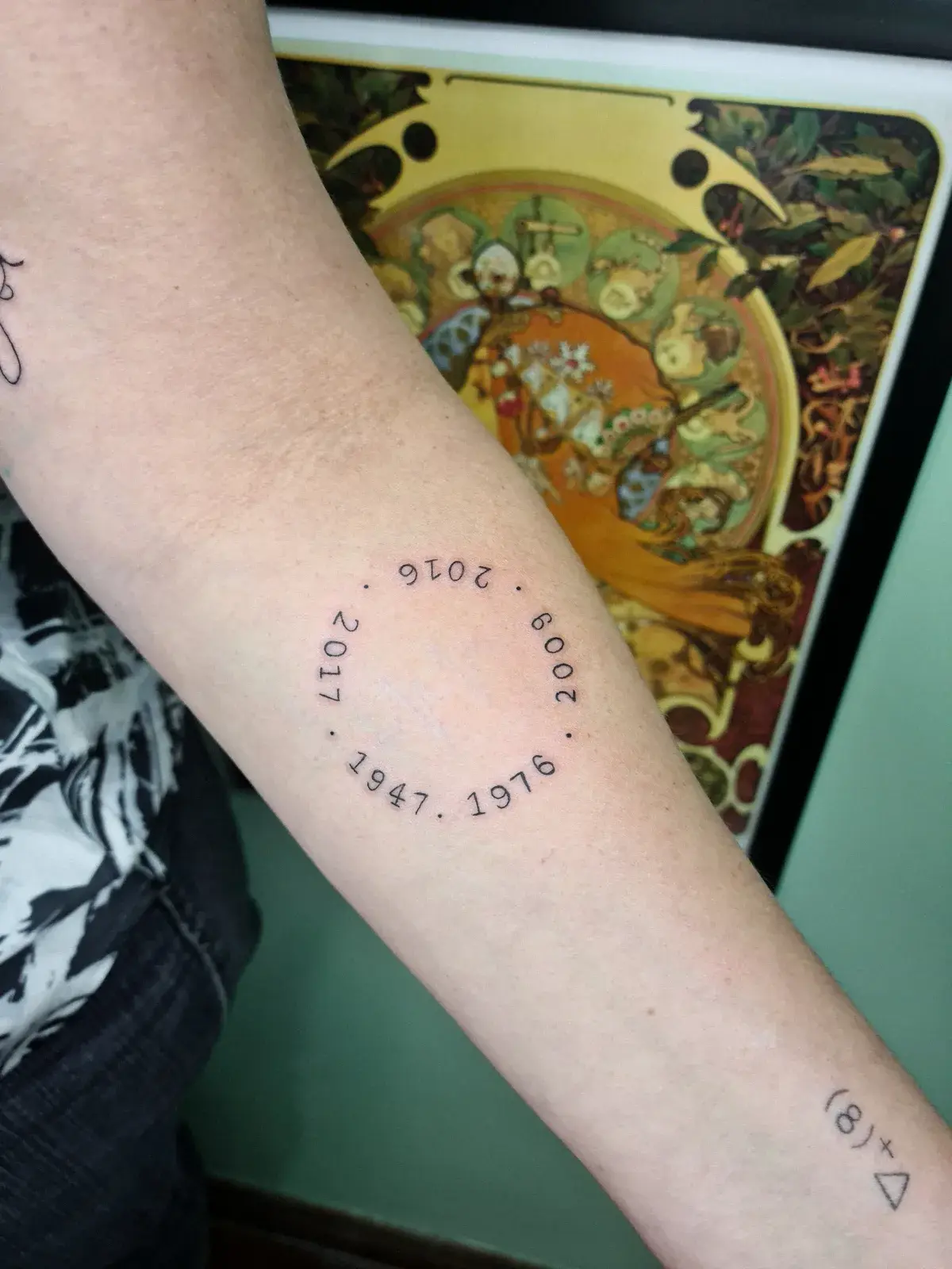 Tatuagem fine line com datas dispostas em círculo no antebraço
