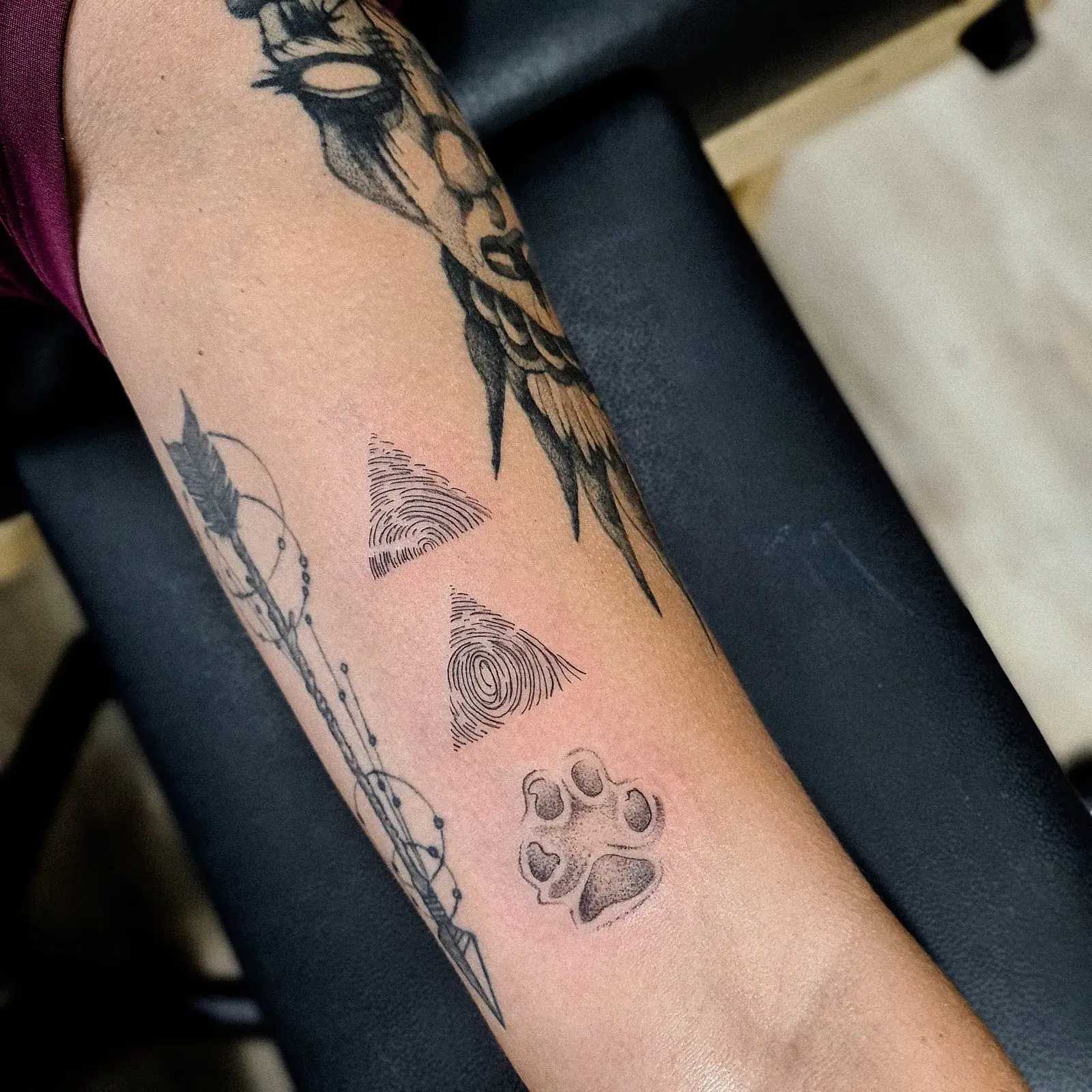 Tatuagem fine line com digitais dentro de triângulos e patinha de cachorro, no antebraço