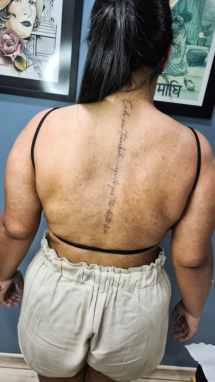 Tatuagem fine line com escrita vertical descendo pela coluna, nas costas