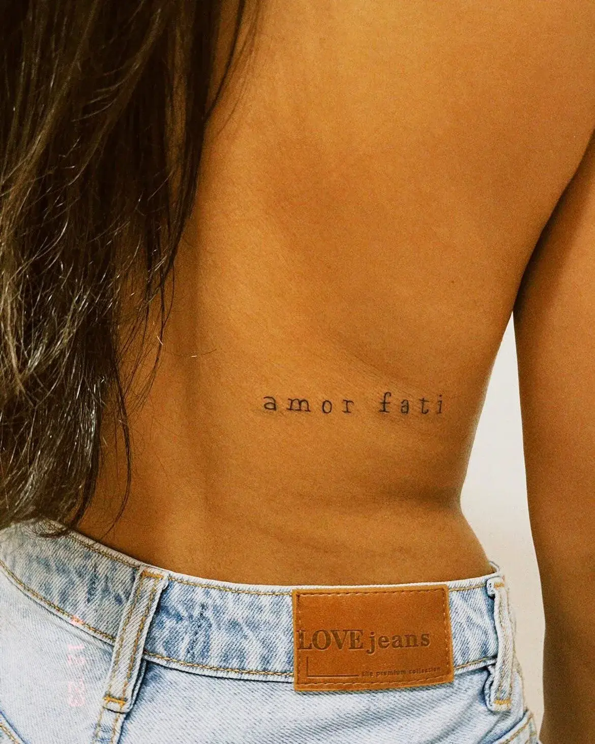 Tatuagem fine line com o lettering amor fati na lombar