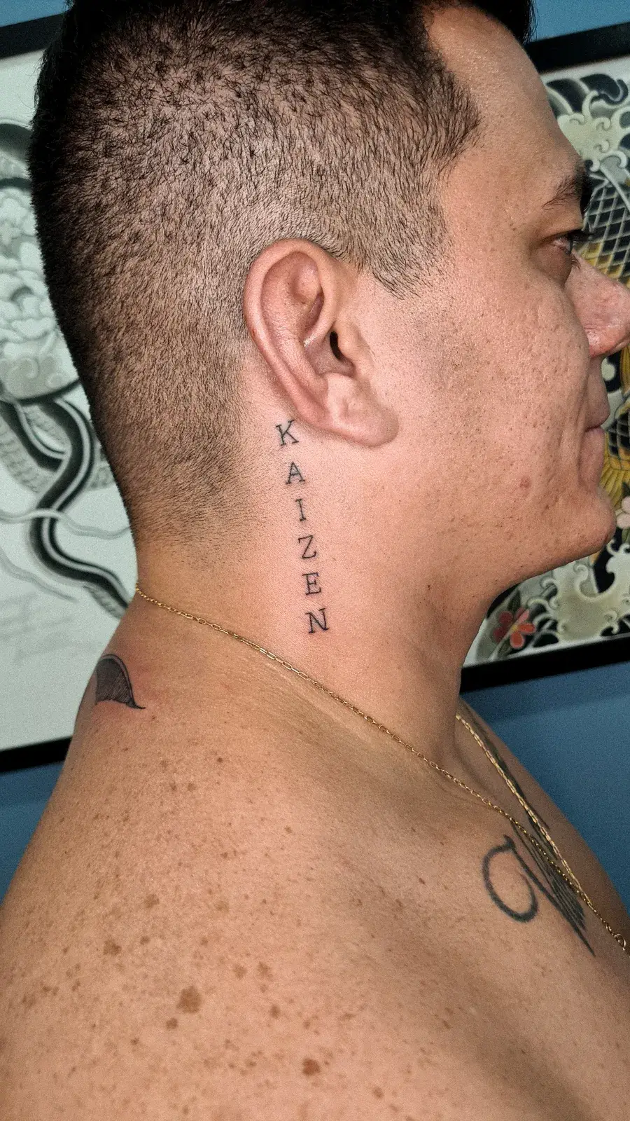 Tatuagem fine line com o lettering Kaizen na vertical, no pescoço