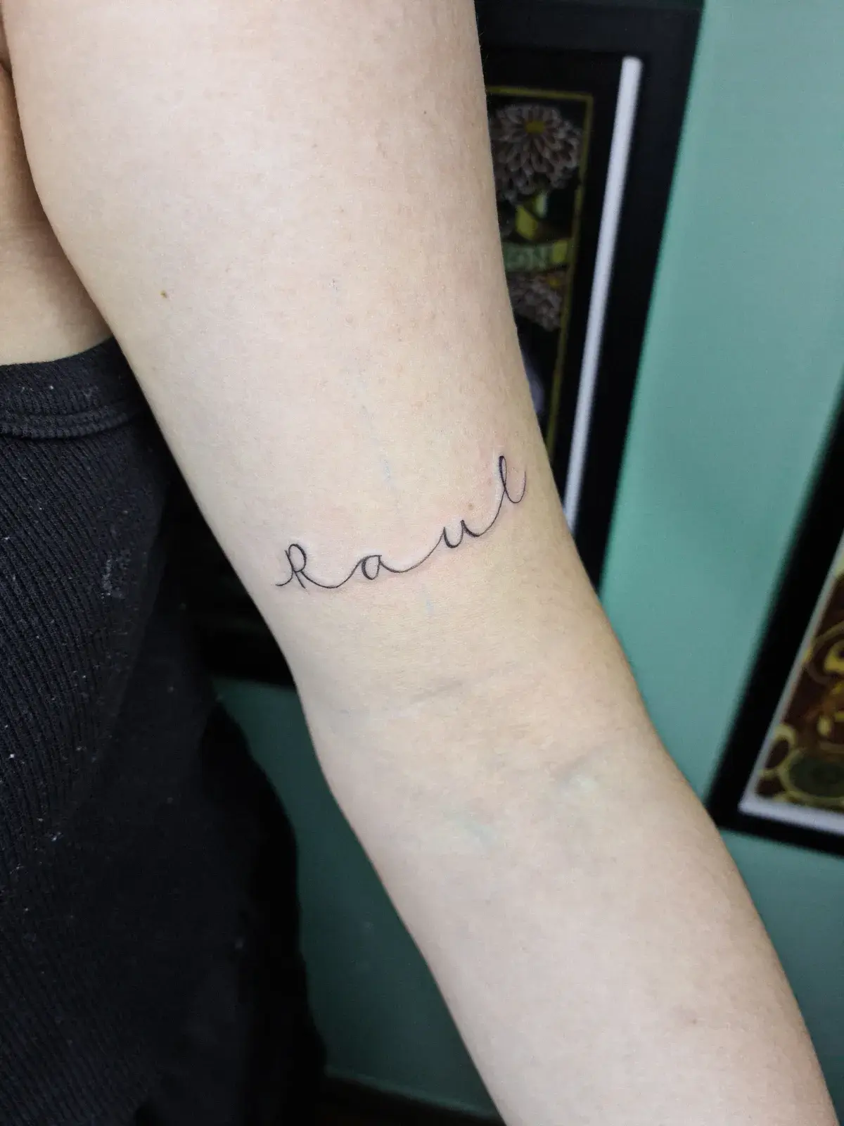 Tatuagem fine line com um nome em cursiva contornando o braço