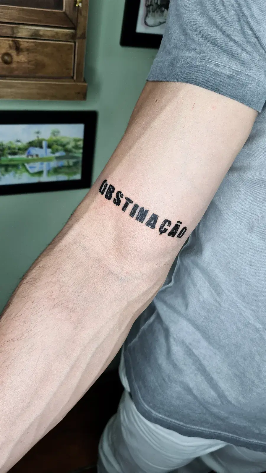 Tatuagem fine line com o lettering Obstinação no antebraço