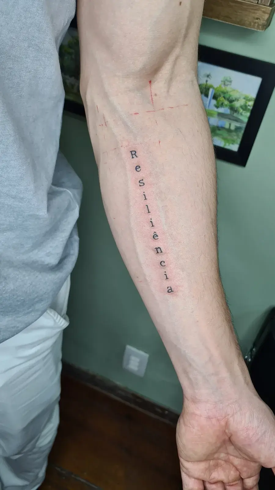 Tatuagem fine line com o lettering Resiliência na vertical, no antebraço