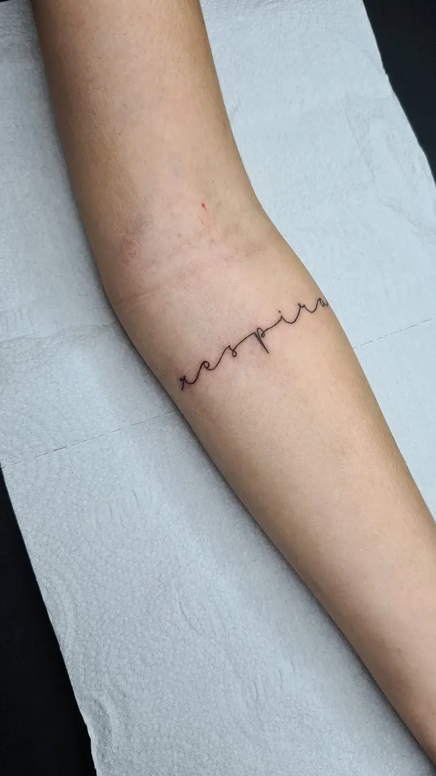 Tatuagem fine line com o lettering respira contornando o punho