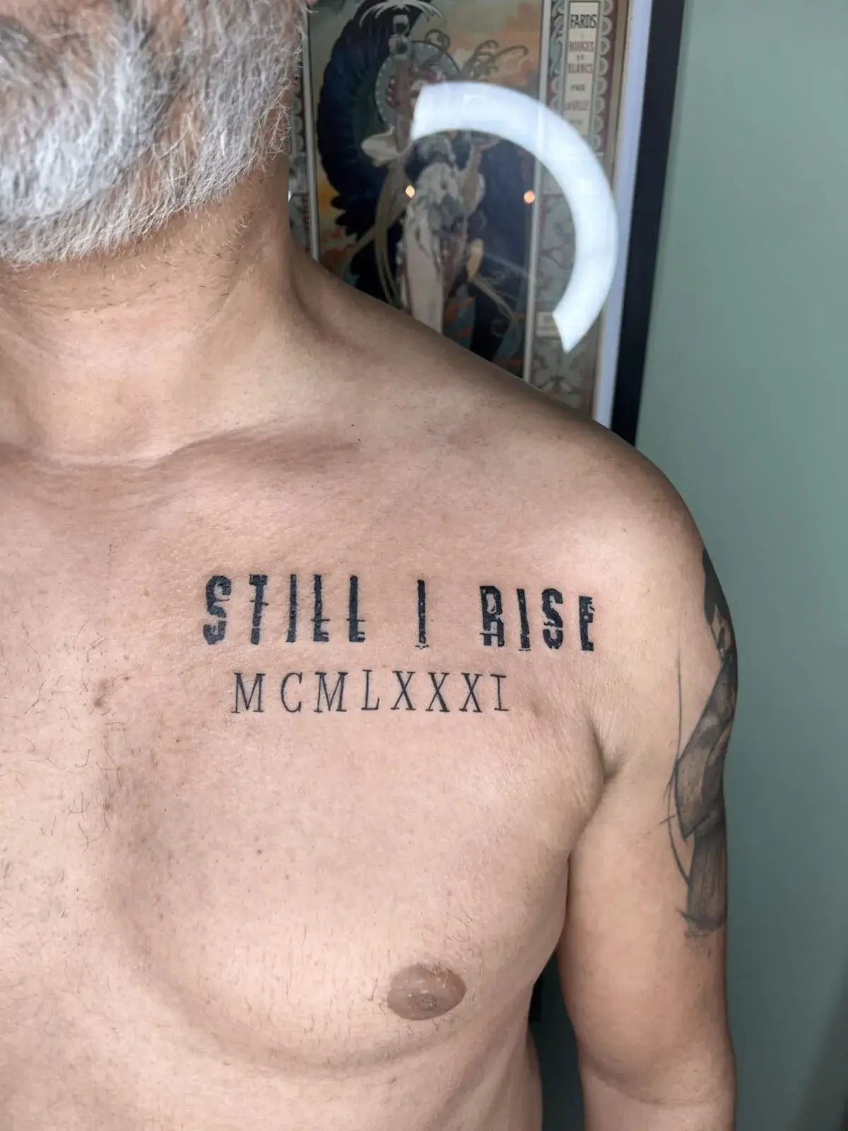 Tatuagem fine line com o lettering Still I Rise e uma data em algarismos romanos, no peito