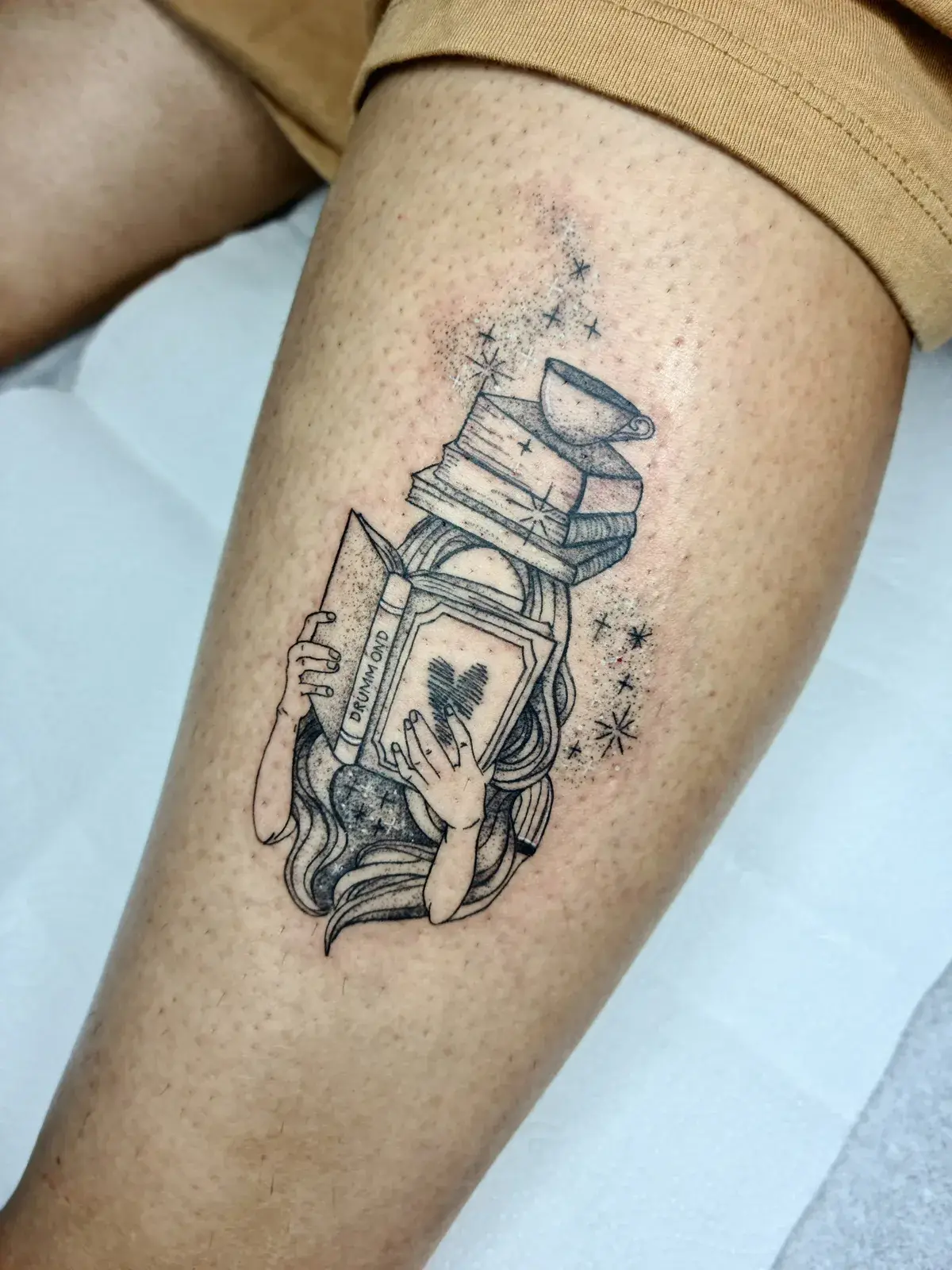 Tatuagem fine line de pilha de livros, cartola e cartas na coxa