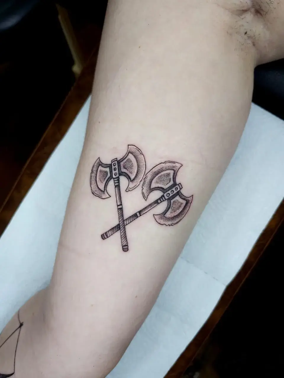 Tatuagem fine line de dois machados cruzados em pontilhismo no antebraço