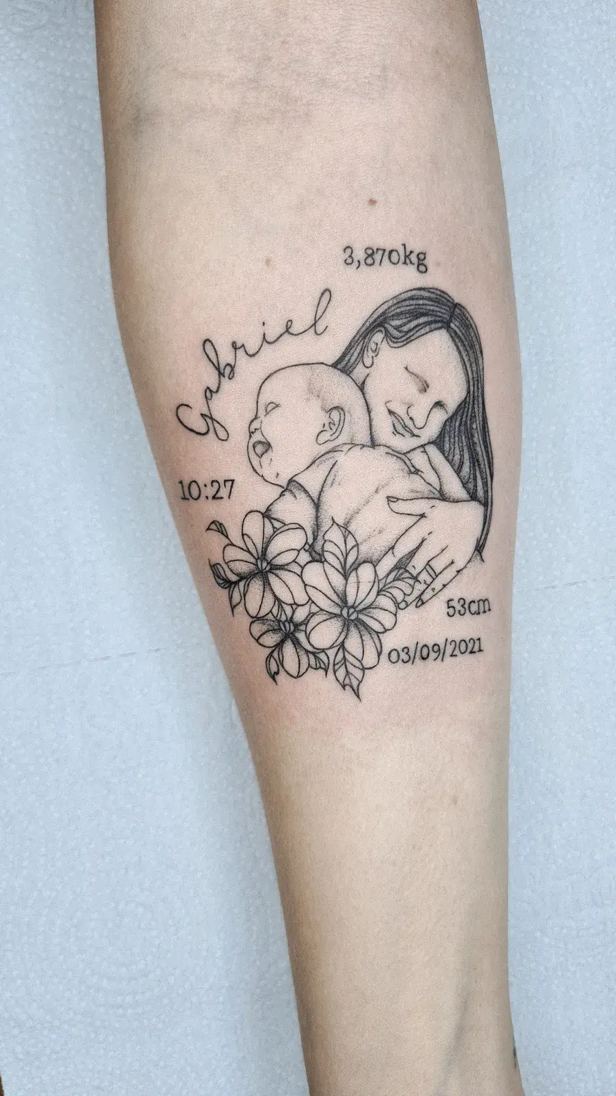 Tatuagem fine line de mãe com bebê, flores e dados de nascimento, no antebraço
