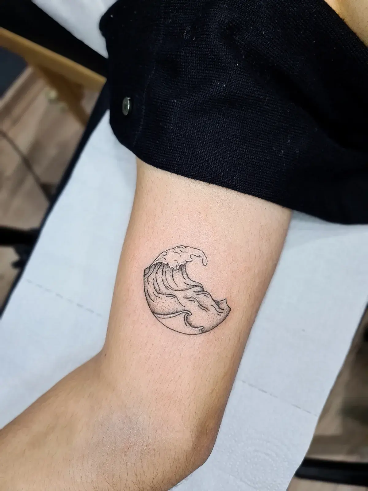 Tatuagem fine line de onda dentro de um círculo, em pontilhismo no braço