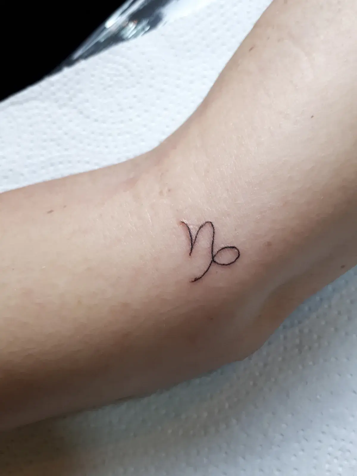 Tatuagem fine line com o símbolo de Capricórnio em traço contínuo no braço