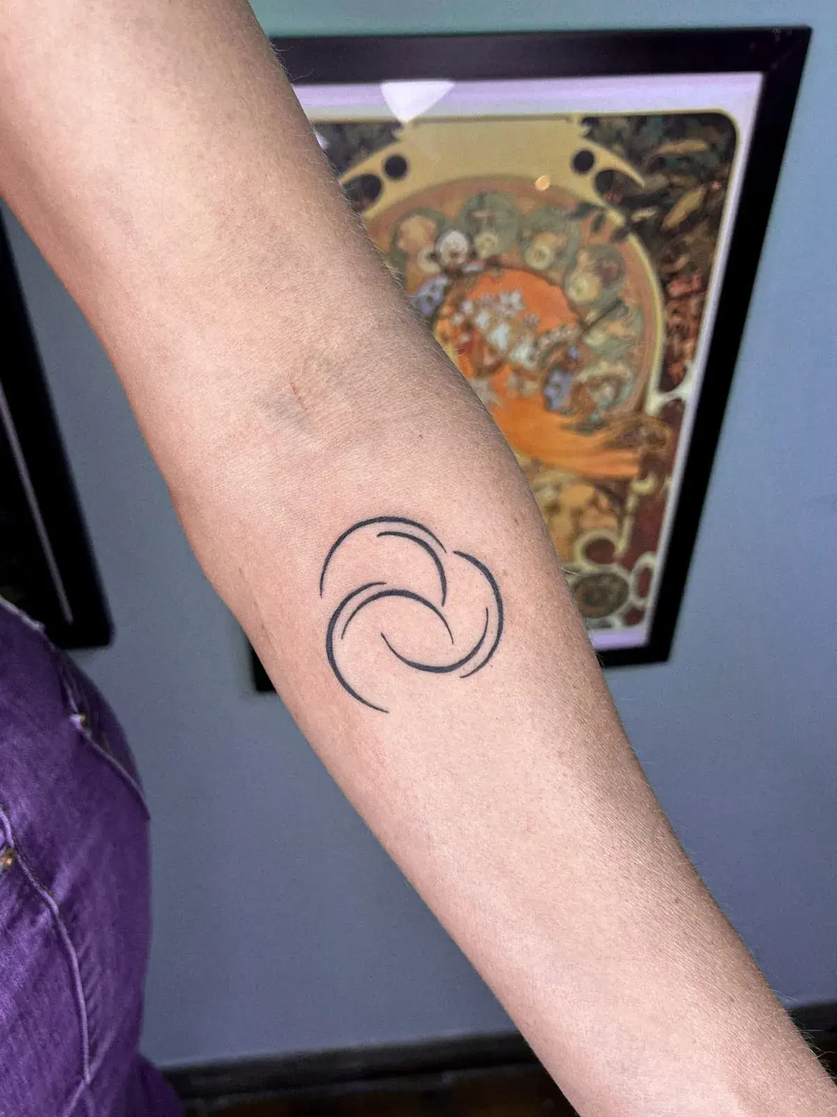 Tatuagem fine line de símbolo com três espirais dentro de um círculo, no antebraço