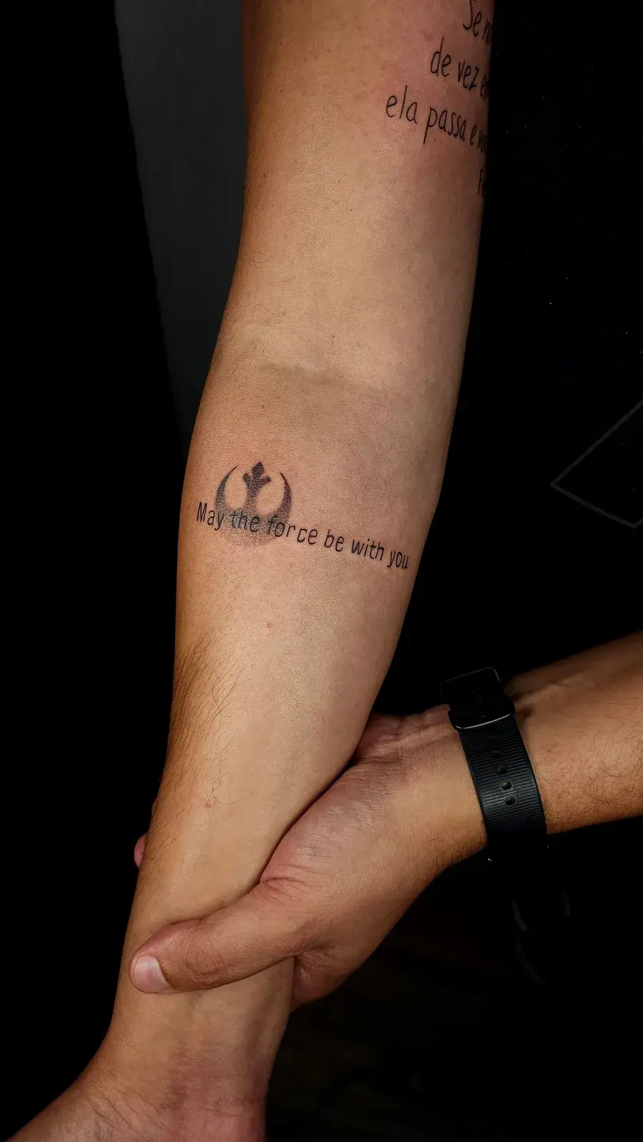 Tatuagem fine line do símbolo da Aliança Rebelde, de Star Wars, com a frase May the force be with you, no antebraço