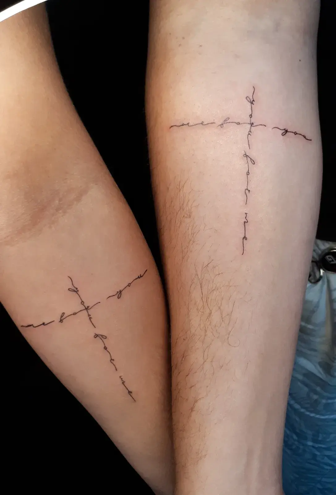 Tatuagem de casal em fine line, com cruz formada por galhos no antebraço de duas pessoas
