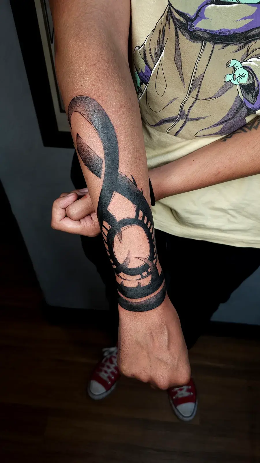 Tatuagem geek com o símbolo de Baldur’s Gate em preto sólido contornando o antebraço