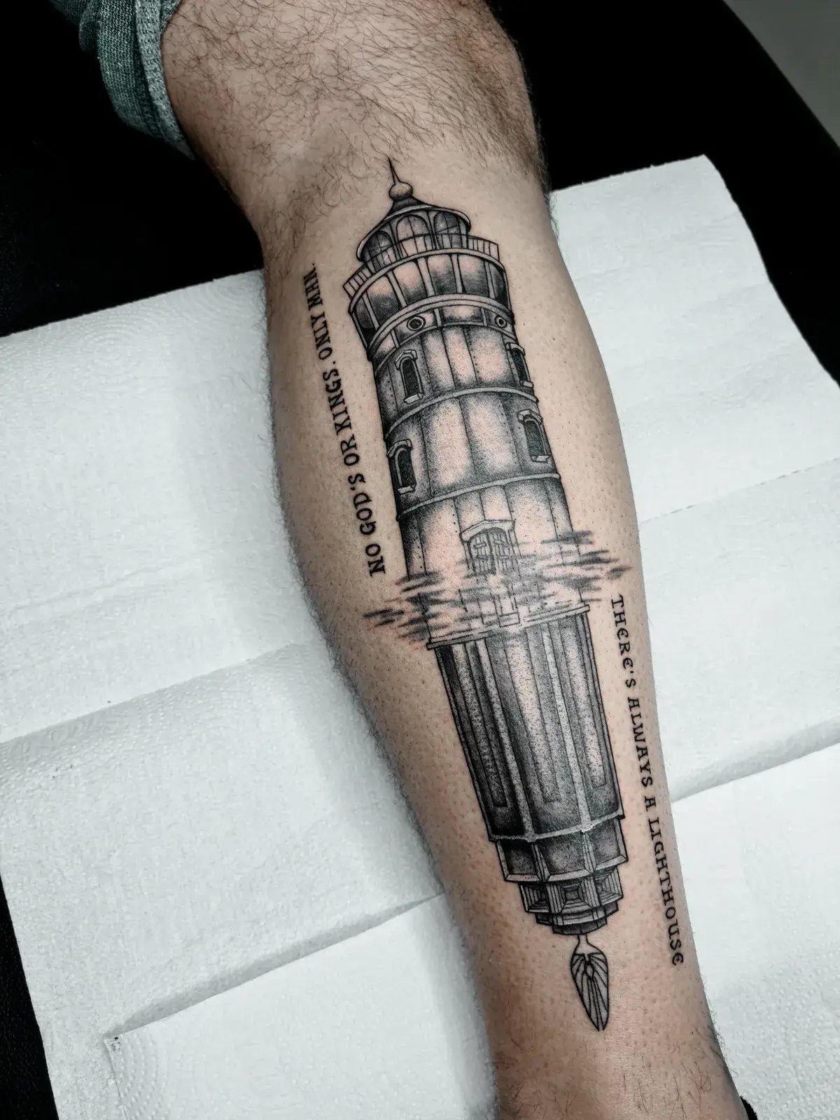 Tatuagem geek de BioShock com farol e a frase No gods or kings, only man, em pontilhismo na panturrilha