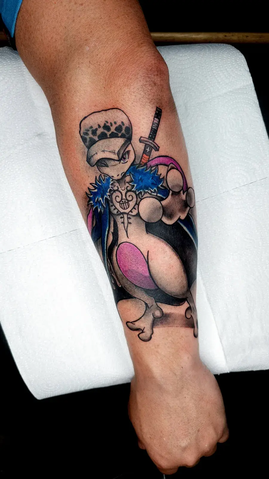 Tatuagem geek em crossover de Mewtwo com Trafalgar Law, de One Piece, em cores no antebraço