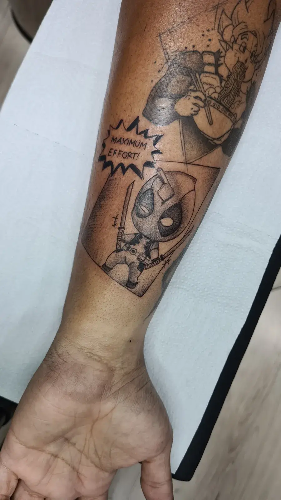 Tatuagem geek do Deadpool em quadro de história em quadrinhos com a legenda Maximum Effort, no antebraço