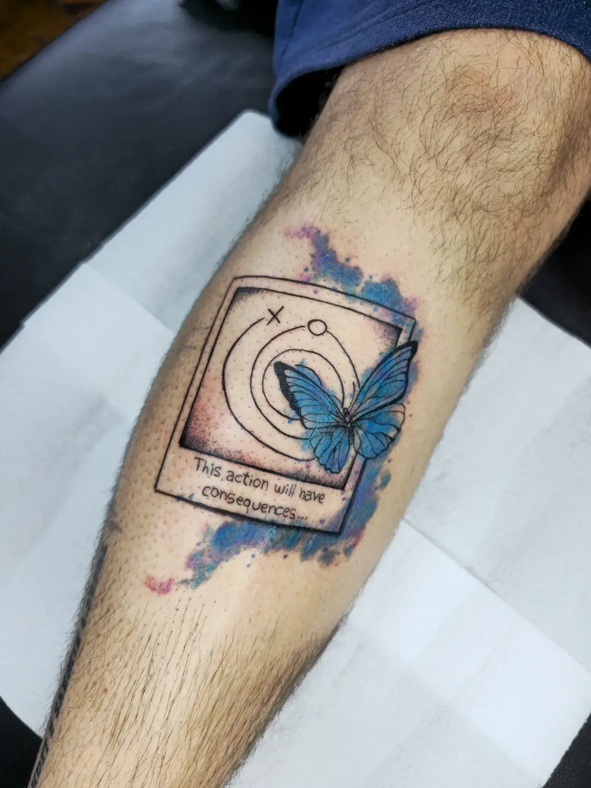 Tatuagem geek de Life is Strange com polaroid e borboleta azul em aquarela, na panturrilha