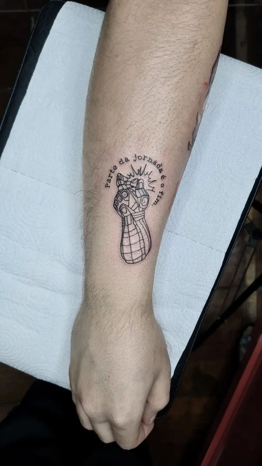 Tatuagem geek da Manopla do Infinito em traço fino com a frase Parte da jornada é o fim, no antebraço
