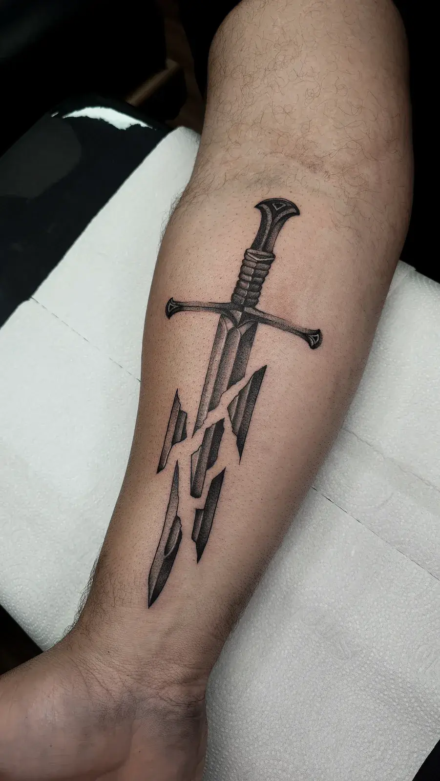 Tatuagem geek da espada Narsil, de O Senhor dos Anéis, em preto e cinza no antebraço