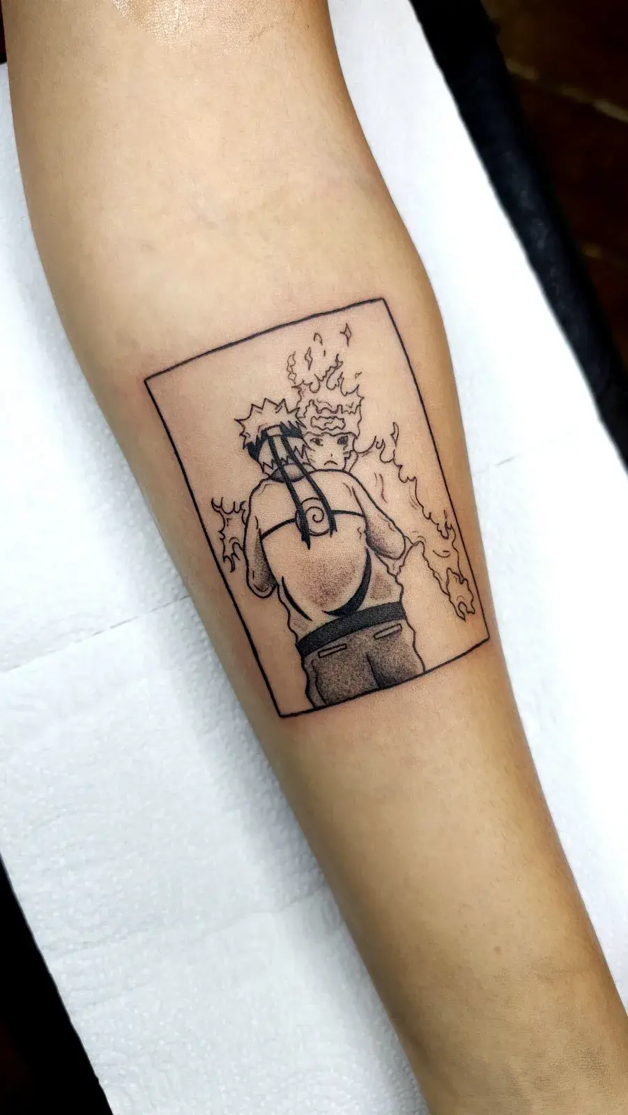 Tatuagem geek de Naruto em quadro com chakra em chamas, em traço fino no antebraço