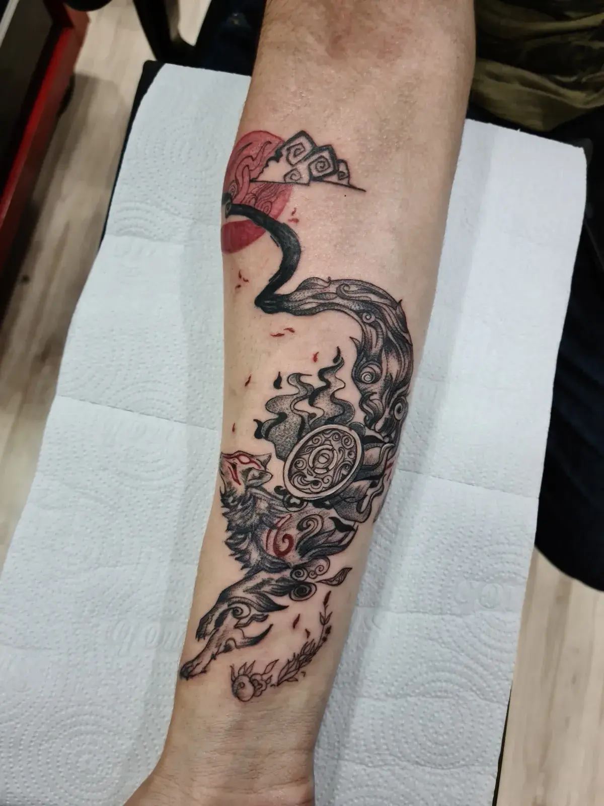 Tatuagem geek da Amaterasu, de Okami, com detalhes em vermelho no antebraço