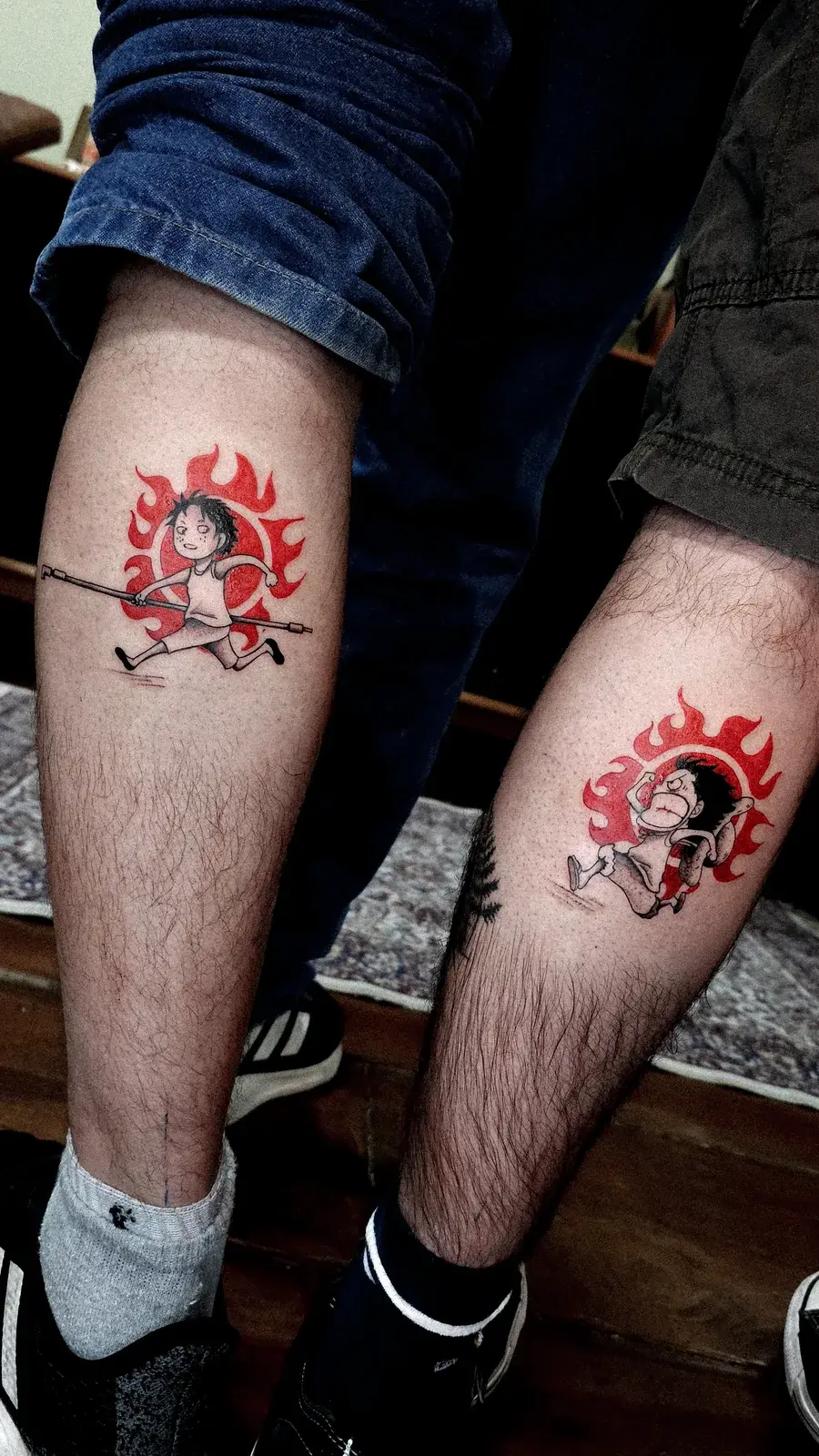Tatuagem geek de One Piece com Ace e Luffy em círculos de chamas vermelhas, na panturrilha