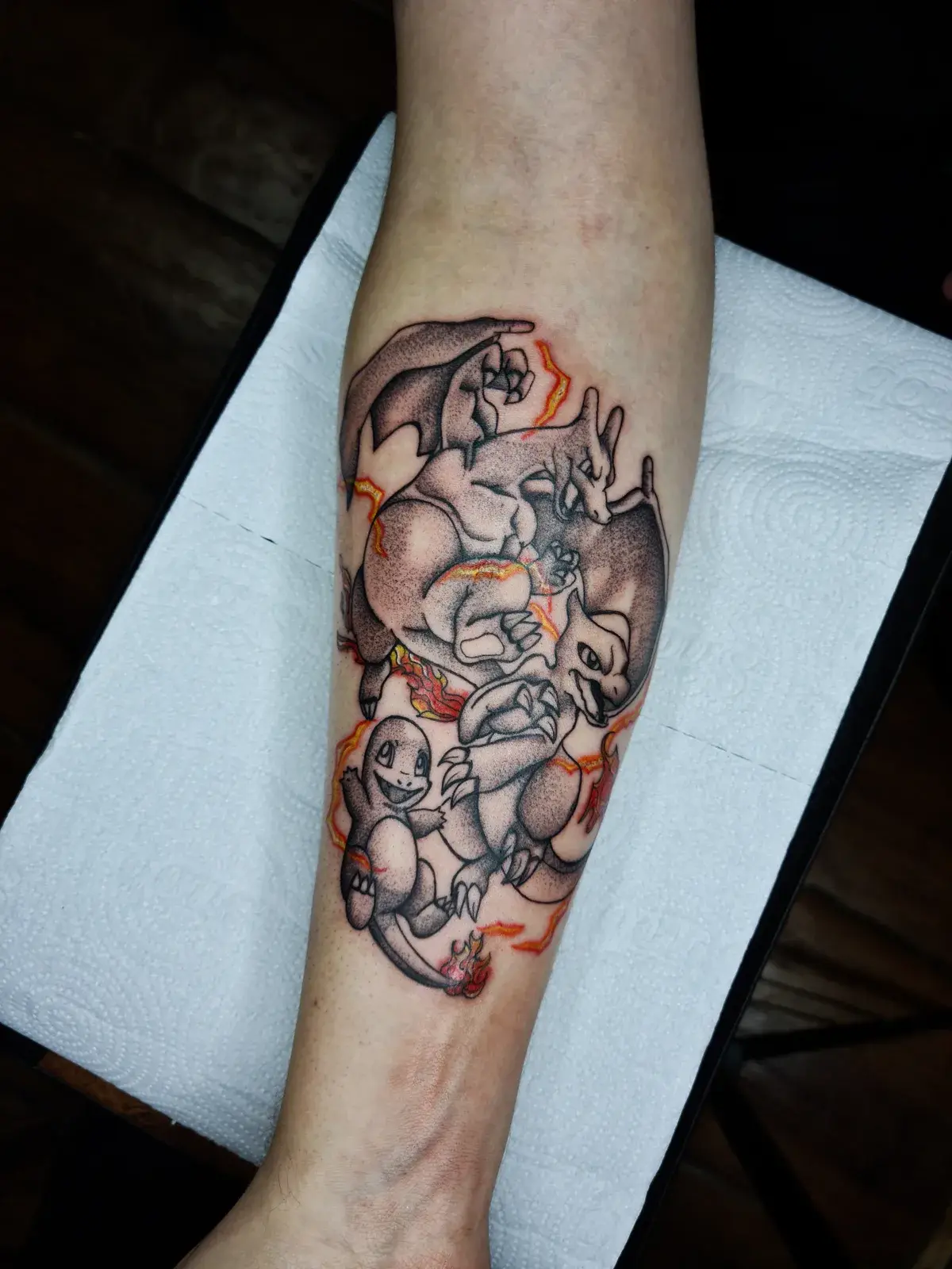 Tatuagem geek de Pokémon com Charmander, Charmeleon e Charizard e chamas em laranja, no antebraço